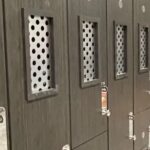 Row of dark gray lockers featuring rectangular, perforated metal ventilation panels.
