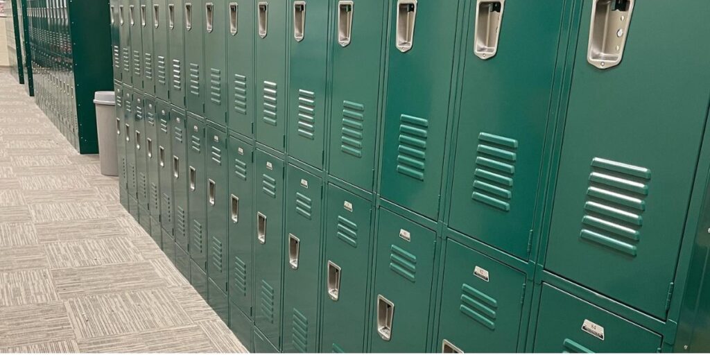 A long bank of tan metal lockers in two tiers along a wall with light-colored tile flooring.