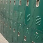 A long bank of tan metal lockers in two tiers along a wall with light-colored tile flooring.