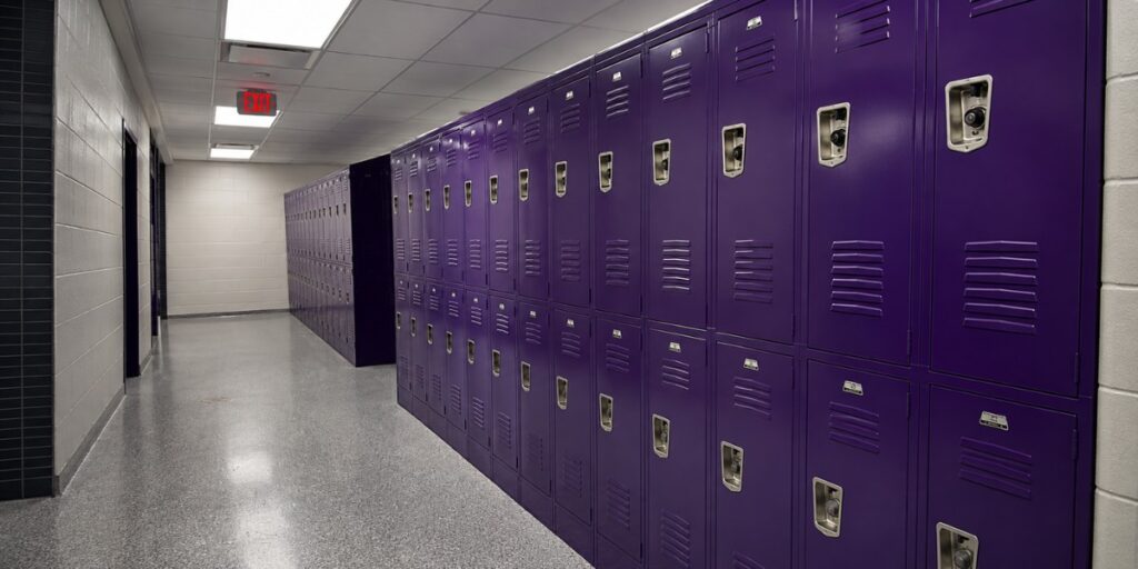 Bright school hallway with rows of purple lockers, polished floors, and overhead lighting, creating a clean, organized educational environment.