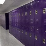 Bright school hallway with rows of purple lockers, polished floors, and overhead lighting, creating a clean, organized educational environment.