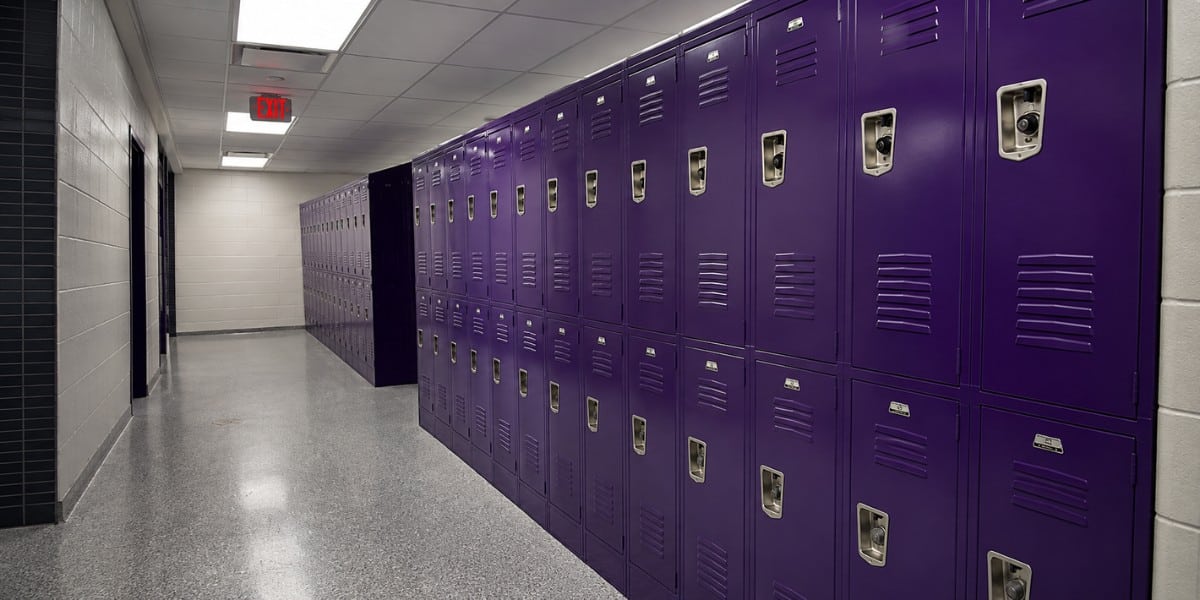 Bright school hallway with rows of purple lockers, polished floors, and overhead lighting, creating a clean, organized educational environment.